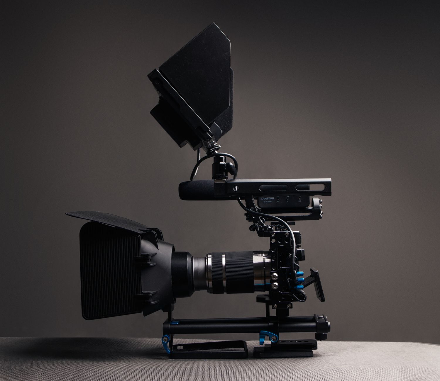 Professional black video camera with lens and monitor and wires placed on desk against gray background in modern studio with equipment