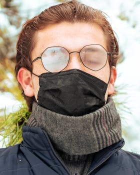 Close-up portrait of a man wearing glasses, face mask, and scarf outdoors in winter.