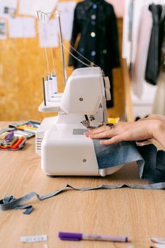Hands operating a sewing machine to stitch denim fabric, with colorful threads nearby.