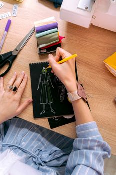 A person sketching a fashion design on a notebook with sewing tools nearby. Creative workspace inspiration.