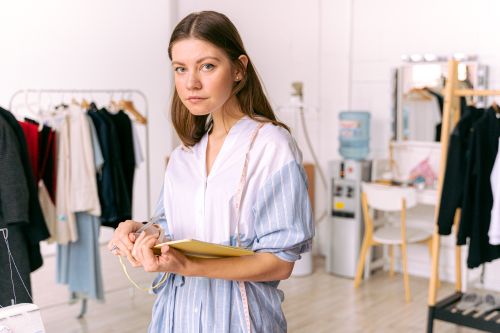Free Fashion designer in studio holding notebook, pondering clothing designs. Stock Photo