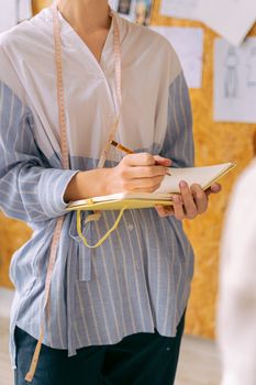 Fashion designer sketching in a creative workspace wearing a sewing pattern tape.