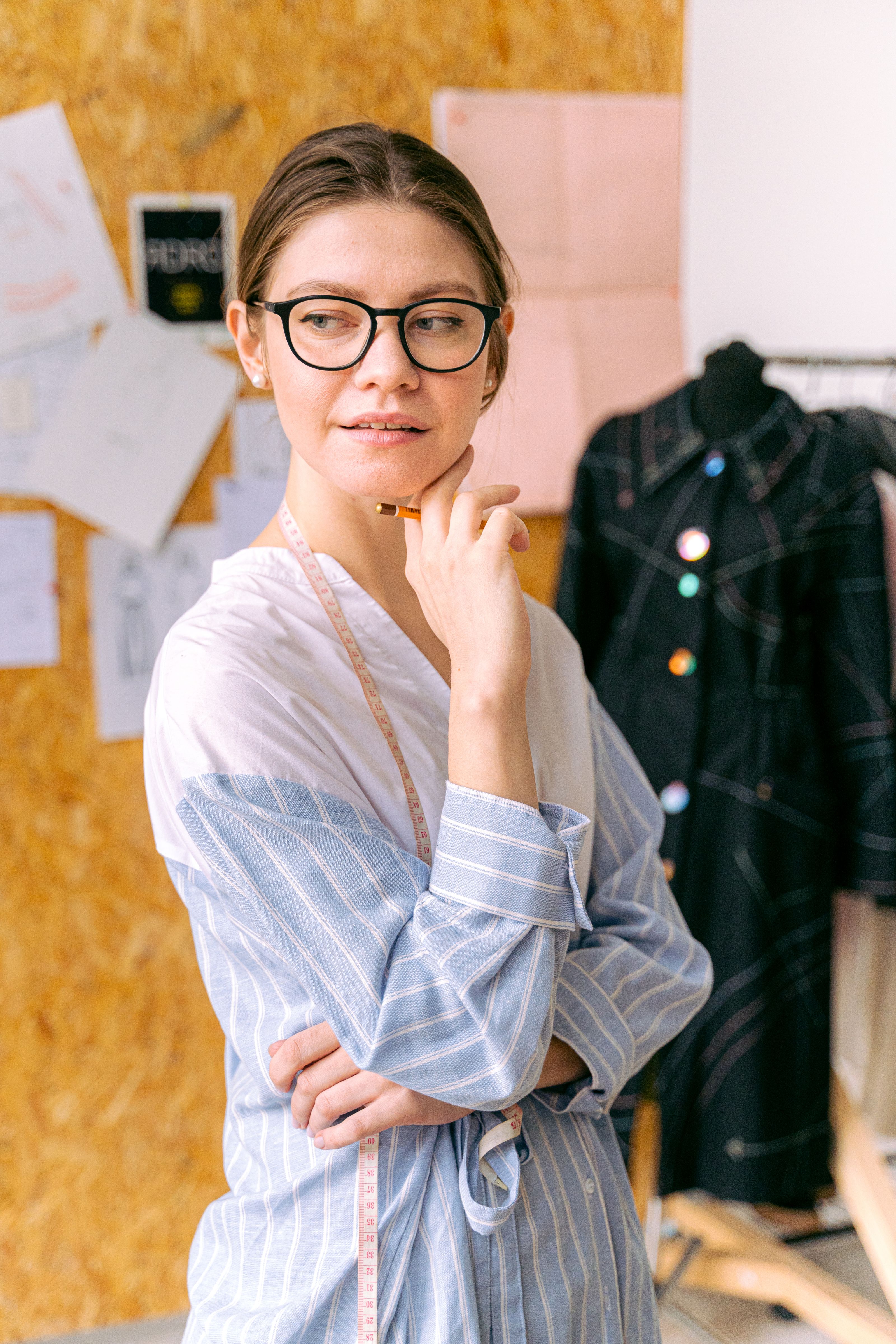 Uma designer de moda pensativa usando óculos, contemplando sua próxima criação em um elegante estúdio.
