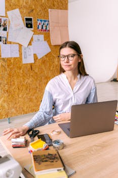 A young professional woman working at a desk in a modern home studio with a laptop.