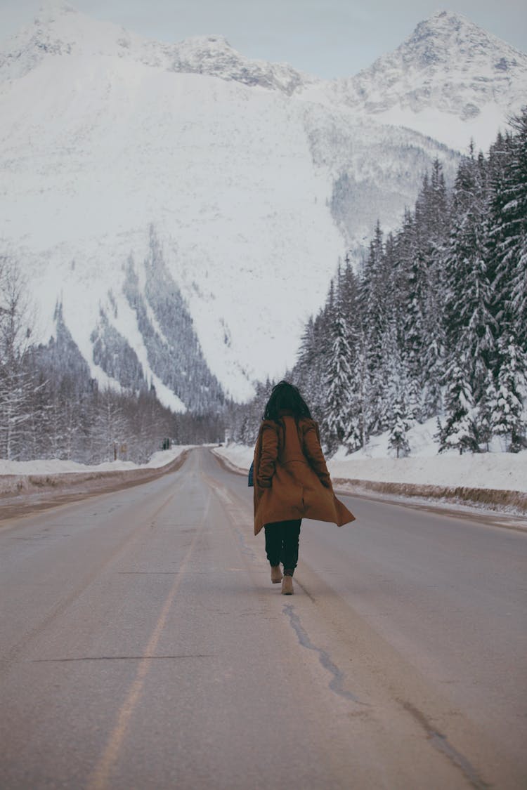 Person Walking In The Middle Of A Road With View Of Snow Covered Mountains