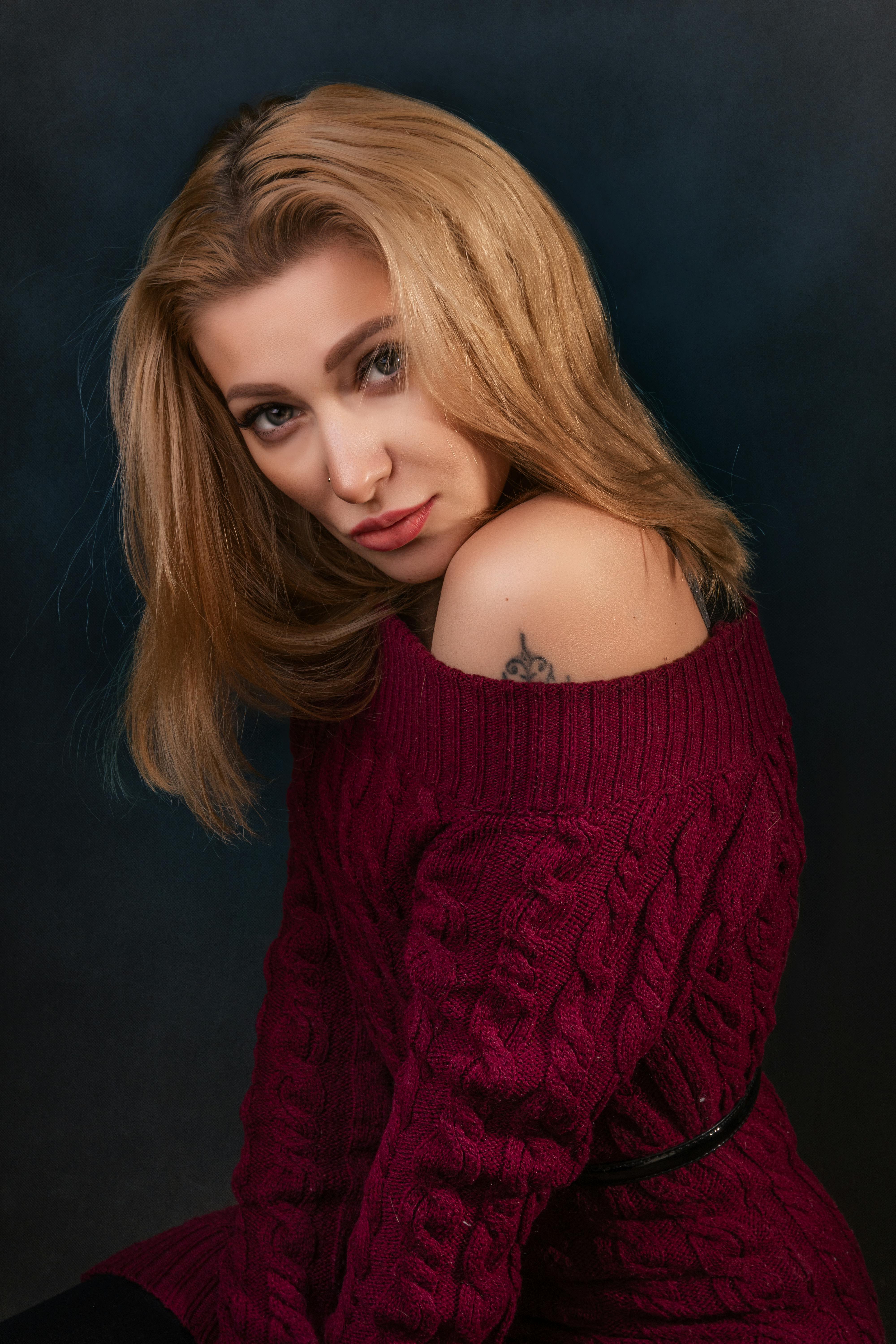 Beautiful portrait of a blonde woman in a maroon knitted sweater in a studio setting.