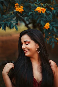 A beautiful woman smiles in front of vibrant yellow flowers, capturing a joyful moment in nature.