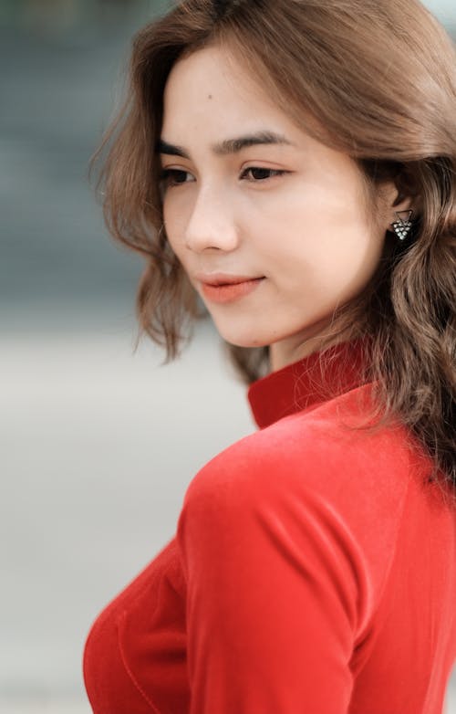 Side view of Asian female with gentle smile wearing red clothes and earrings looking away