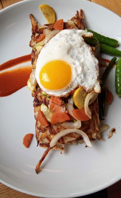 A scoop of crispy diced potatoes and peppers on a griddle beside two fried eggs with runny yolks.