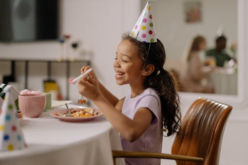 Photograph of a Kid with a Party Hat Smiling while Her Eyes are Closed