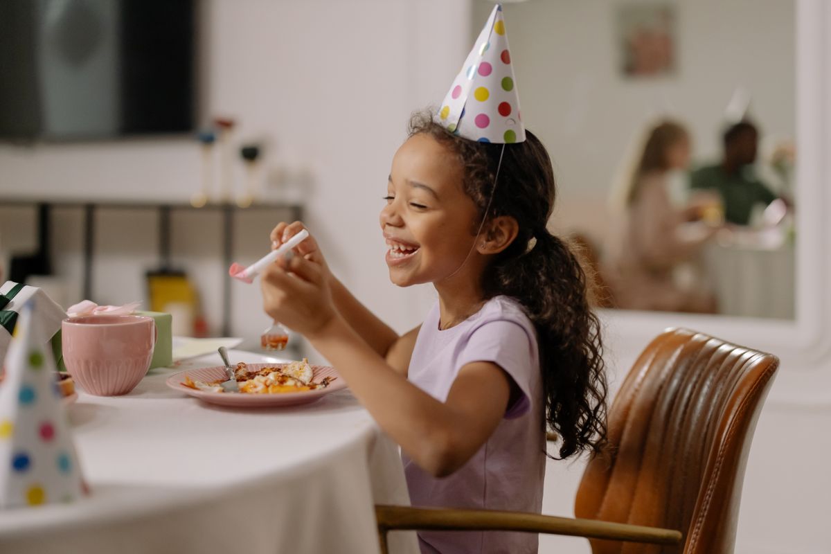Smiling child in a party hat posing with oversized photo booth glasses