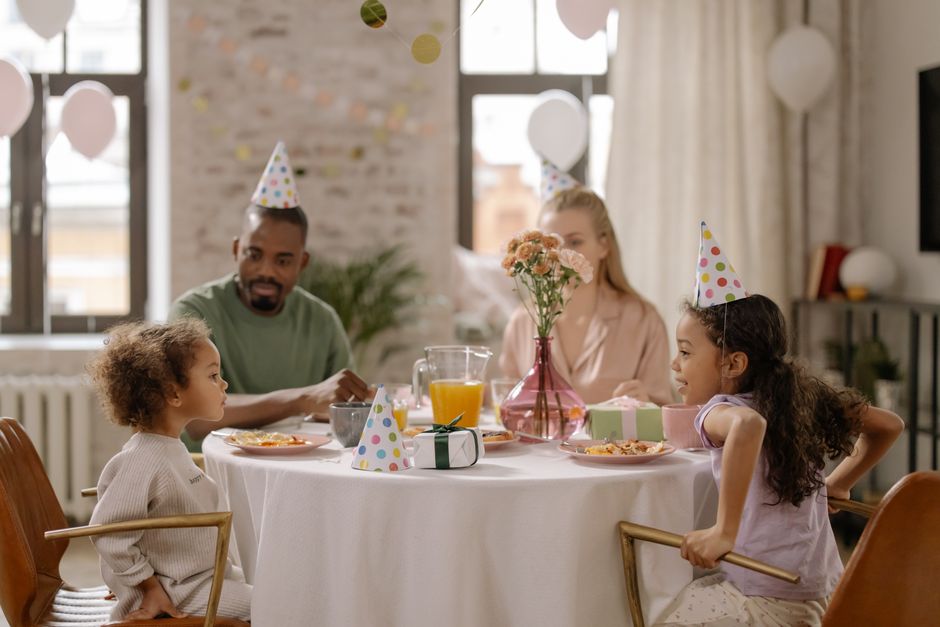 Dark-skinned Nigerian family of four eating a simple meal of rice and beans at a modest wooden dining table inside a Lagos apartment, natural window light streaming in, photorealistic