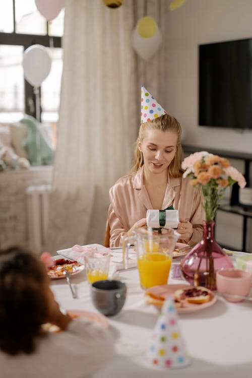 Free A Woman in Pink Long Sleeves Wearing a Party Hat while Holding a Gift Stock Photo