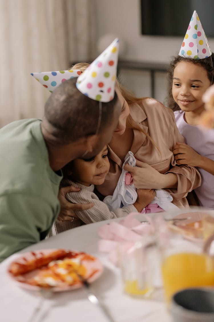 Parents With Children In Party Hats By Table With Food