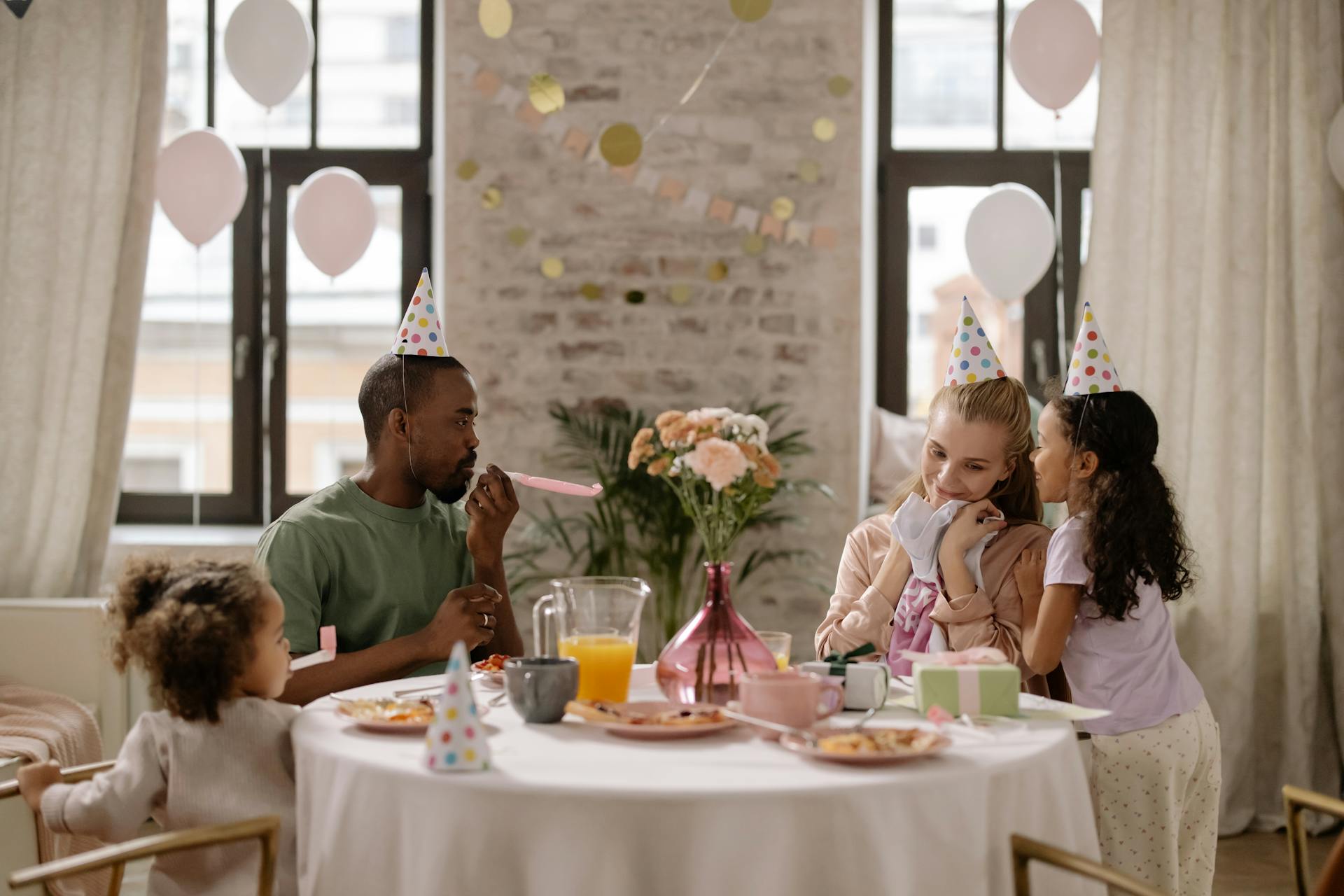 Family gathered indoors for a birthday celebration with decorations, food, and party hats.