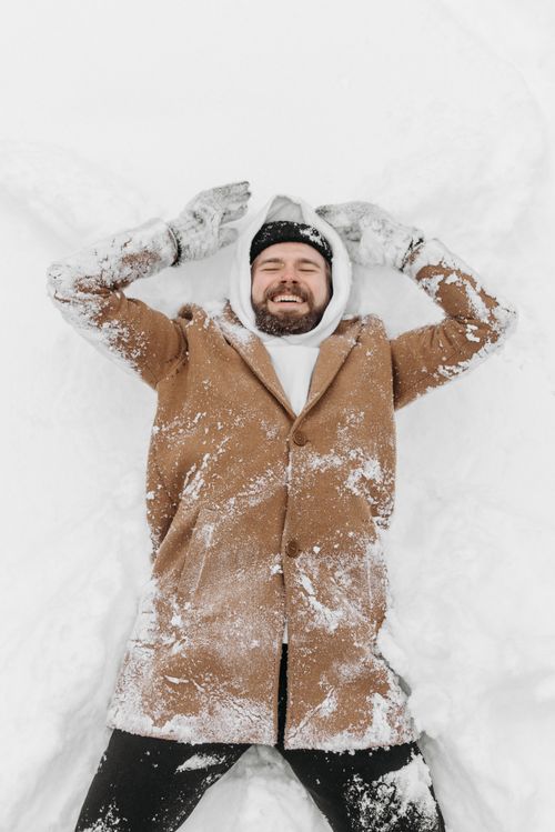Free Smiling man lying in the snow making snow angels, dressed warmly in winter apparel. Stock Photo