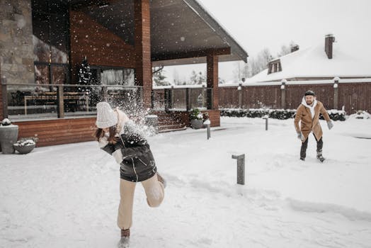 A man and woman enjoy a fun snowball fight in front of a snow-covered cabin during winter.