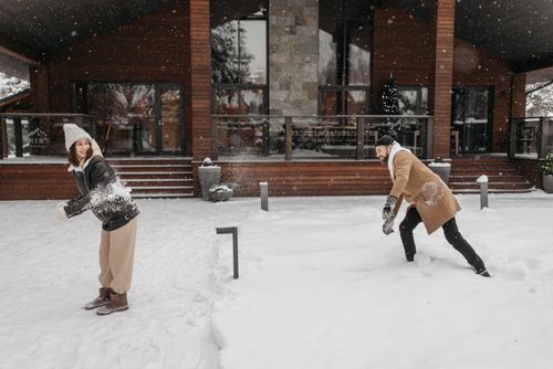 Free A joyful couple having a playful snowball fight in front of a cozy house during winter. Stock Photo