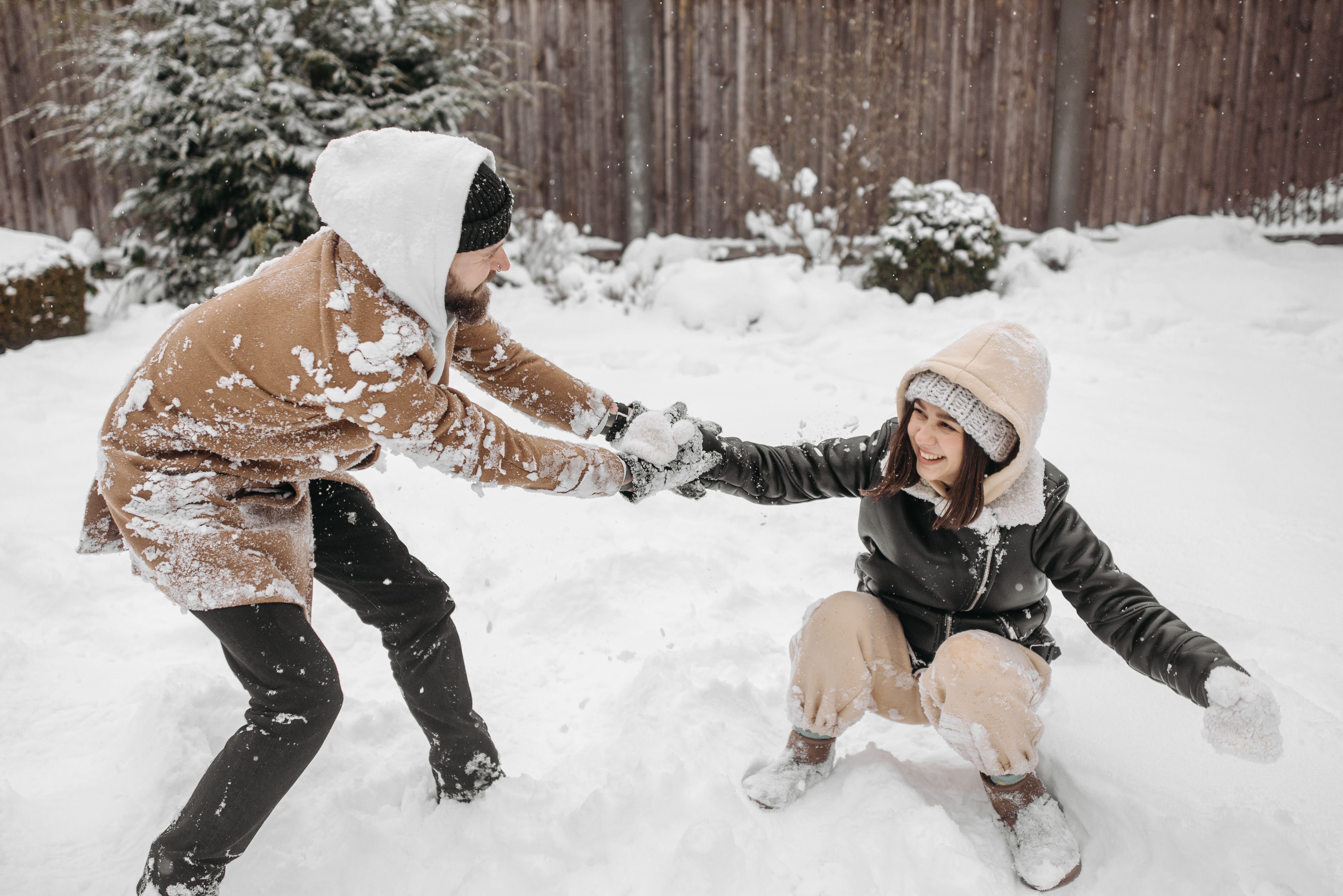 A joyful couple playing in snow, dressed warmly in winter clothes, embracing the cold weather.