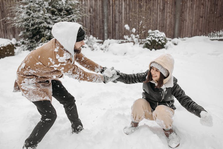 A Couple In Winter Clothes Playing On A Snow Covered Ground