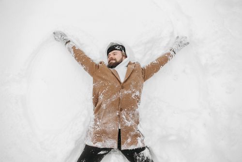 Free Man in winter clothes making snow angel, enjoying winter fun outdoors. Stock Photo
