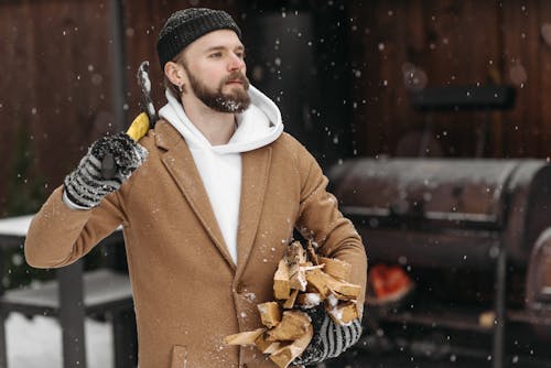 A Man in Brown Coat Holding an Axe and Chopped Woods