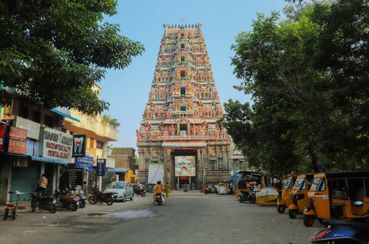 A bustling street view of a colorful Hindu temple in Chennai, India, with auto rickshaws and pedestrians.