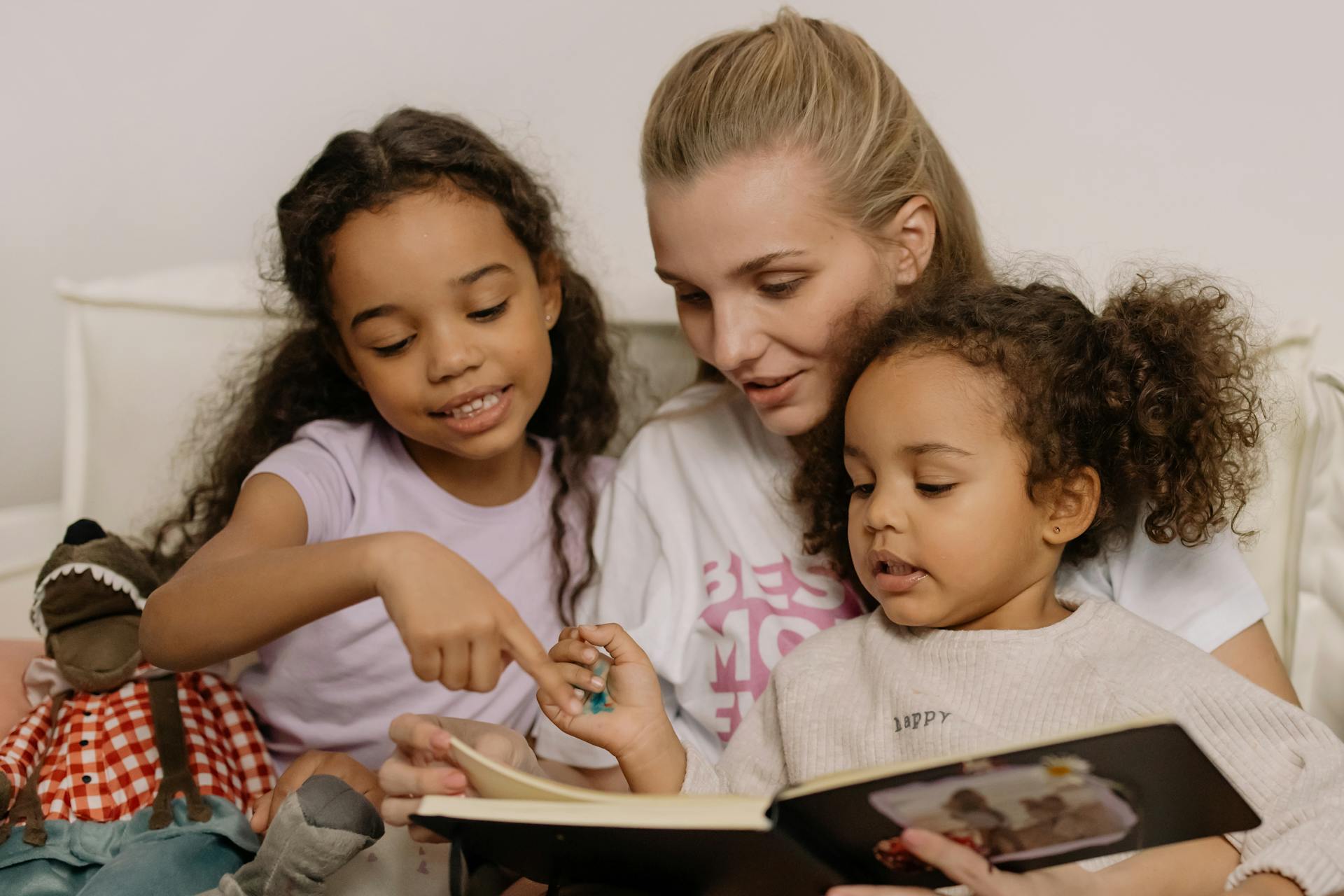 A loving mother and her daughters enjoy quality time sharing a photo album on the couch.