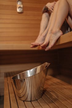 A couple enjoying a relaxing sauna session with a metal bucket in warm wooden surroundings.