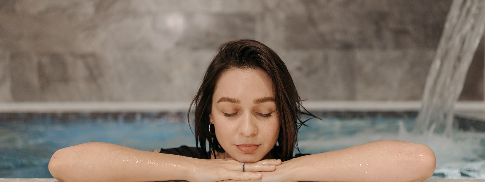 Woman relaxing at a luxurious indoor spa pool with eyes closed, embracing tranquility.