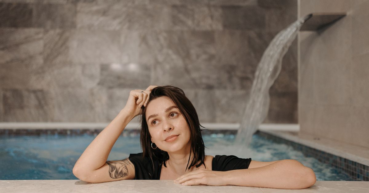 A person in their 40s doing a cold plunge with a look of intense focus, steam rising from the water