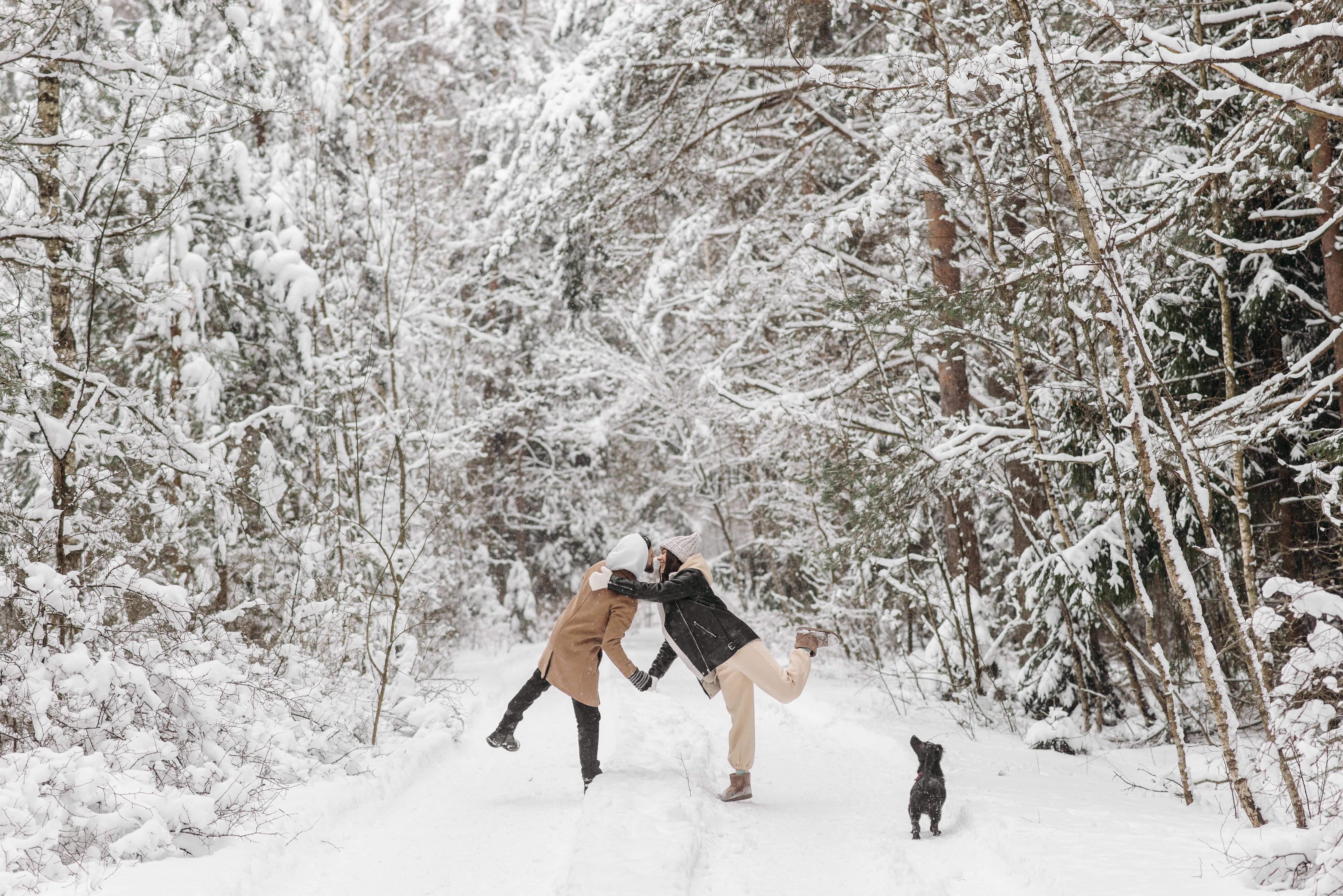 A cheerful couple playing in a snowy forest with their dog on a winter day.