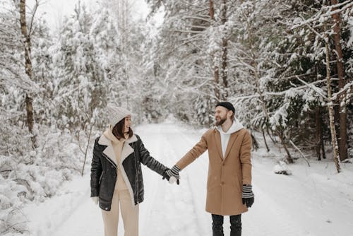 A Couple Holding Hands on a Snow Covered Path in a Forest