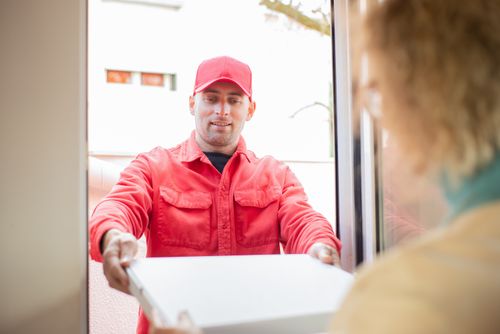 Free A delivery person in red uniform handing over a package at a doorway. Stock Photo