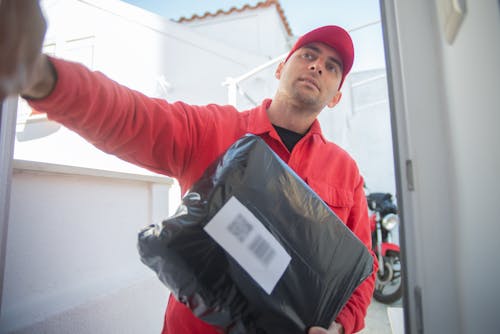 Photograph of a Man with a Red Cap Holding a Black Parcel