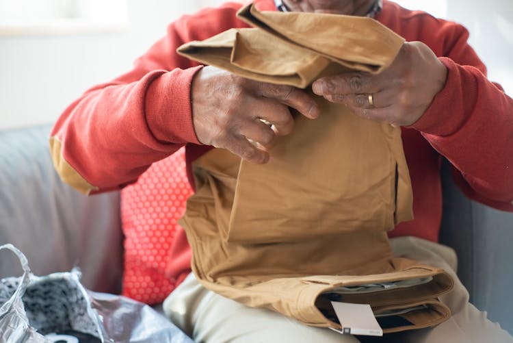 A Person In Red Sweater Folding The Brown Pants While Sitting On A Couch