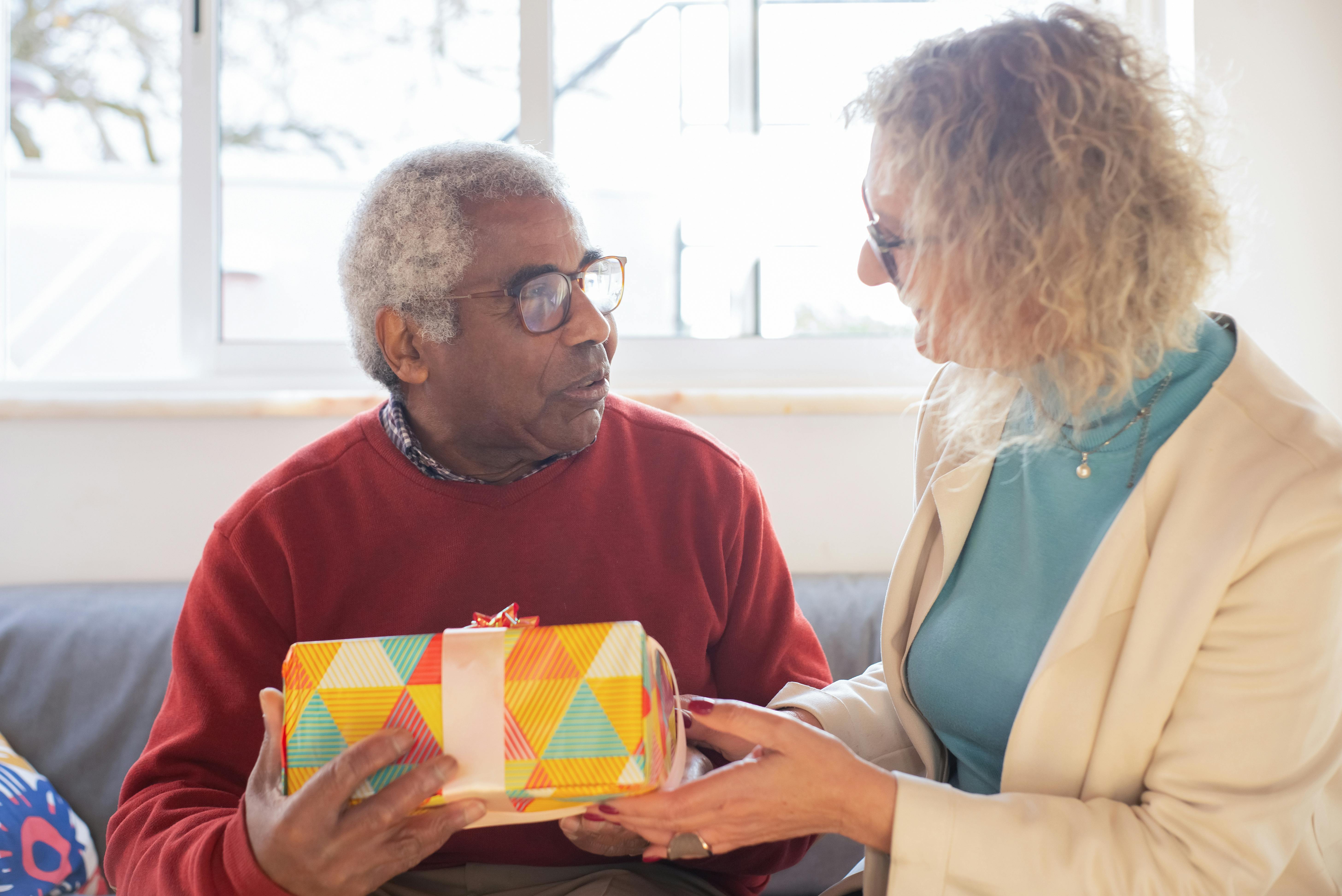 An elderly couple cherishes a special moment exchanging a colorful gift indoors.