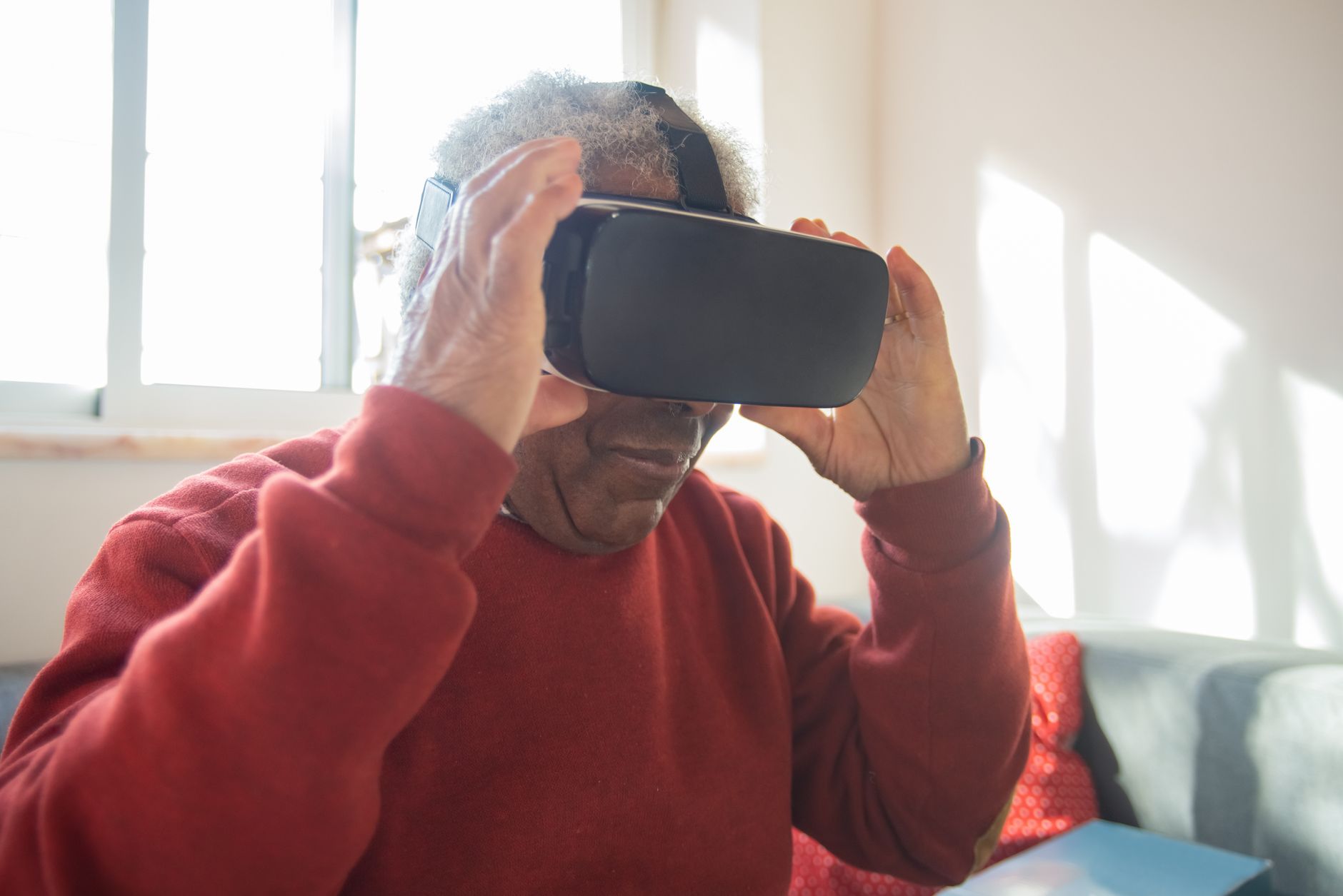 Elderly man in red sweater explores virtual reality using a VR headset indoors.