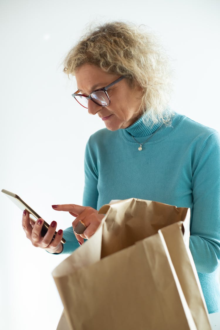 Photograph Of An Elderly Woman Using Her Cell Phone Near A Paper Bag