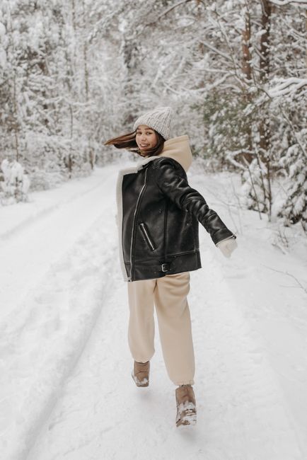 Woman in winter attire walking and smiling through a snowy forest path.