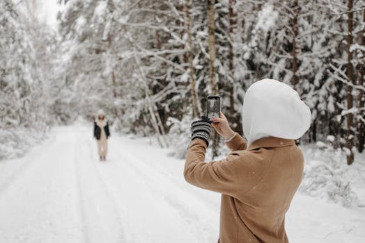A person photographs a snowy forest scene, highlighting winter beauty.