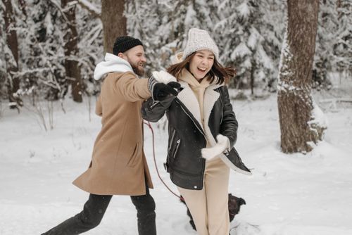Free Happy couple playing in the snow-filled forest with their dog, embracing winter fun. Stock Photo