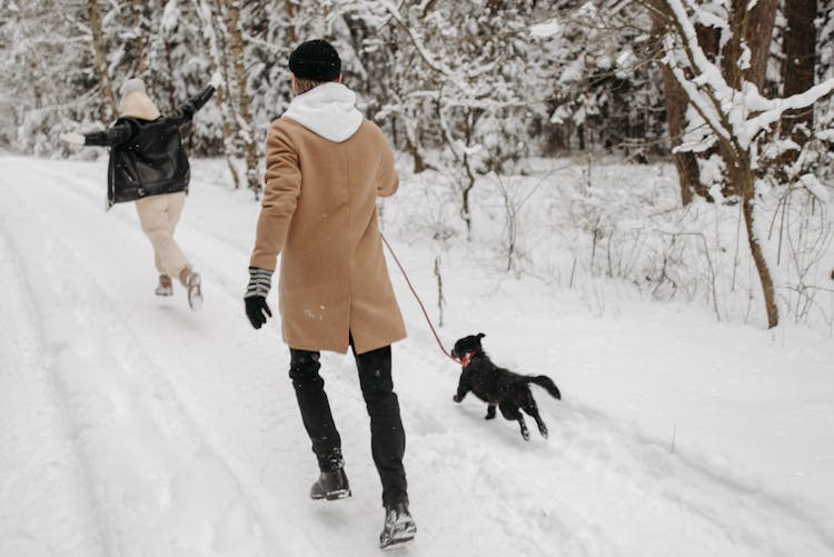 Back View Of A Person In A Brown Coat Running With A Black Dog