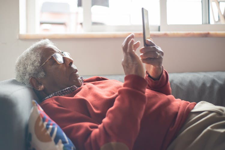 An Elderly Man Using A Cellphone While Lying Down On A Couch