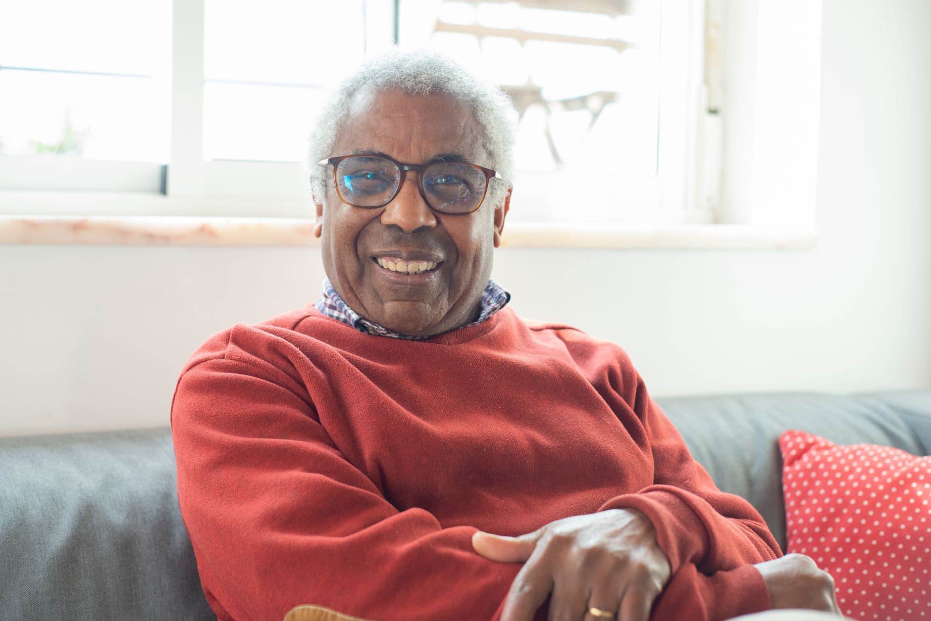 Smiling elderly man in a bright sweater enjoying a relaxing day indoors, sitting comfortably and radiating warmth.