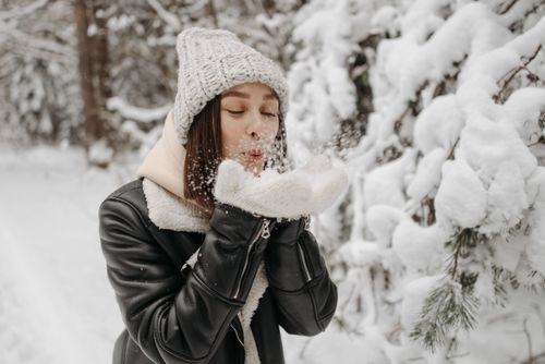 Free Caucasian woman blowing snow in a winter forest, wearing warm clothes. Stock Photo
