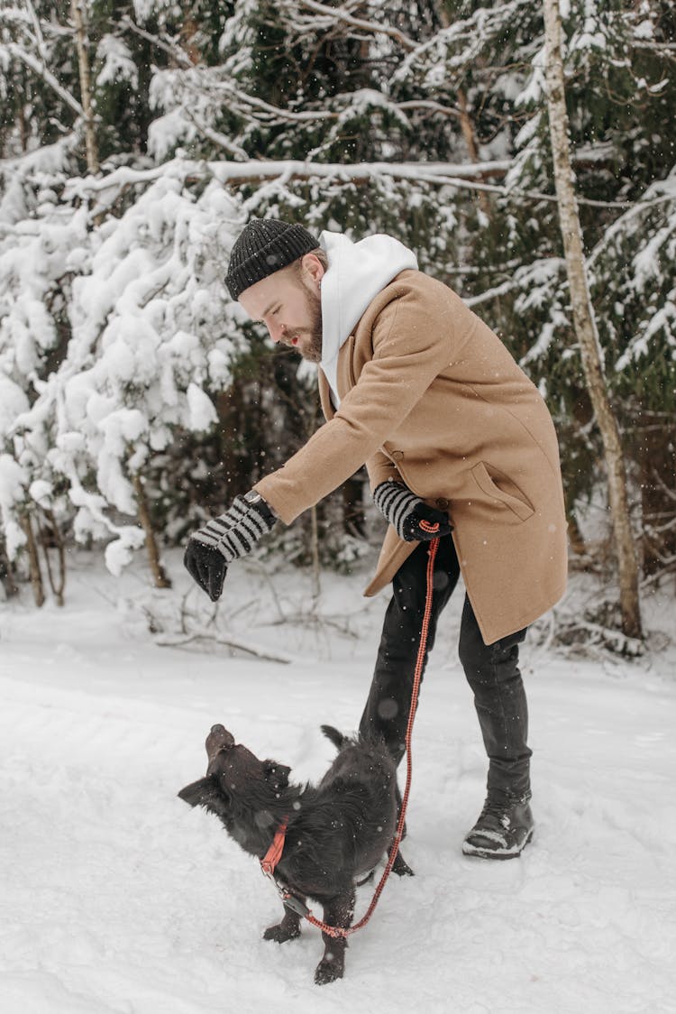 A Man Wearing Winter Clothes Playing With His Dog