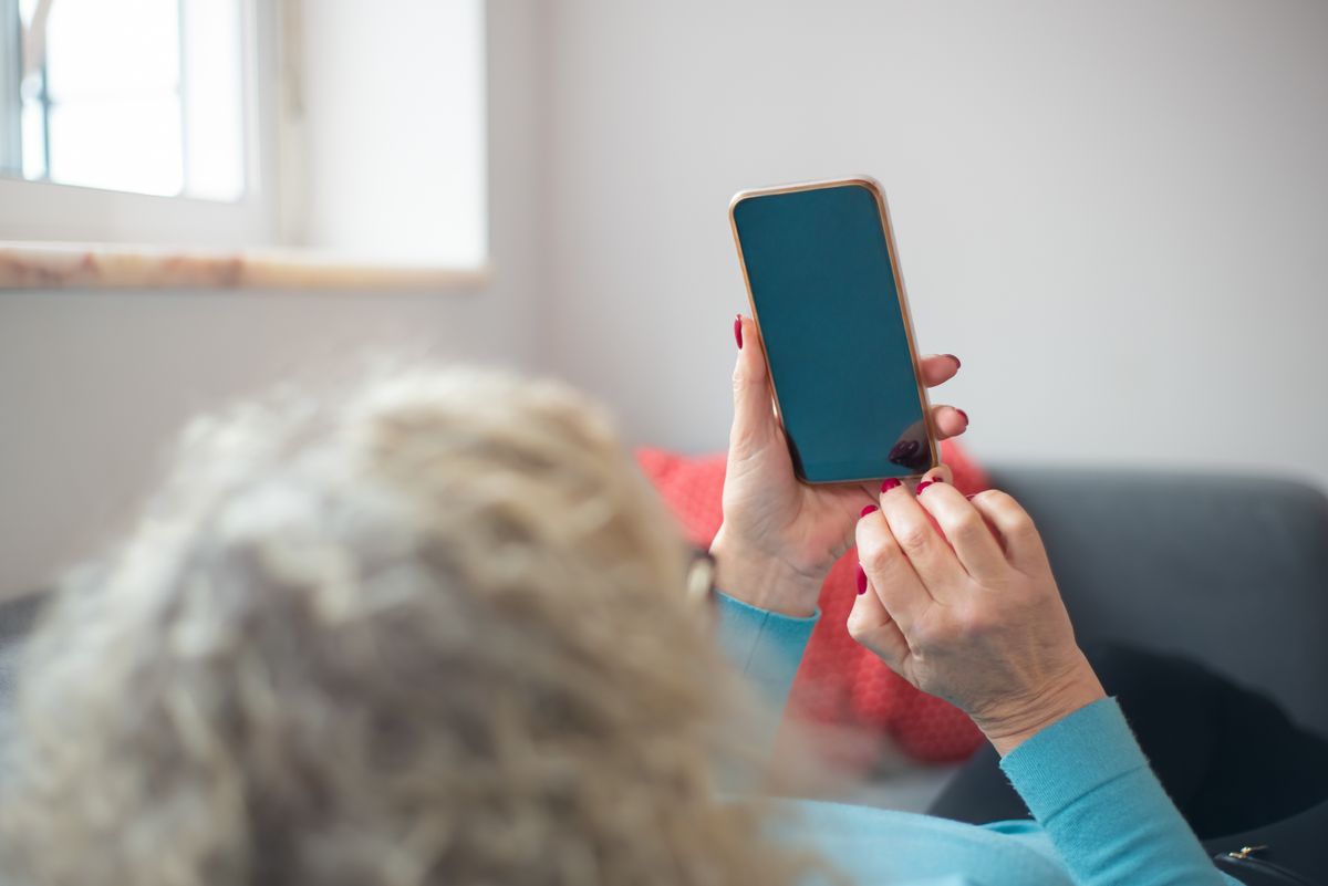 Akıllı telefon ekranına odaklanmış, rahat bir ortamda oturan genç bir kişi