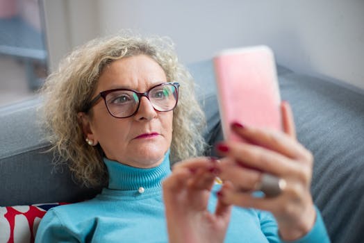 Elderly woman in glasses using smartphone indoors, focused on screen.