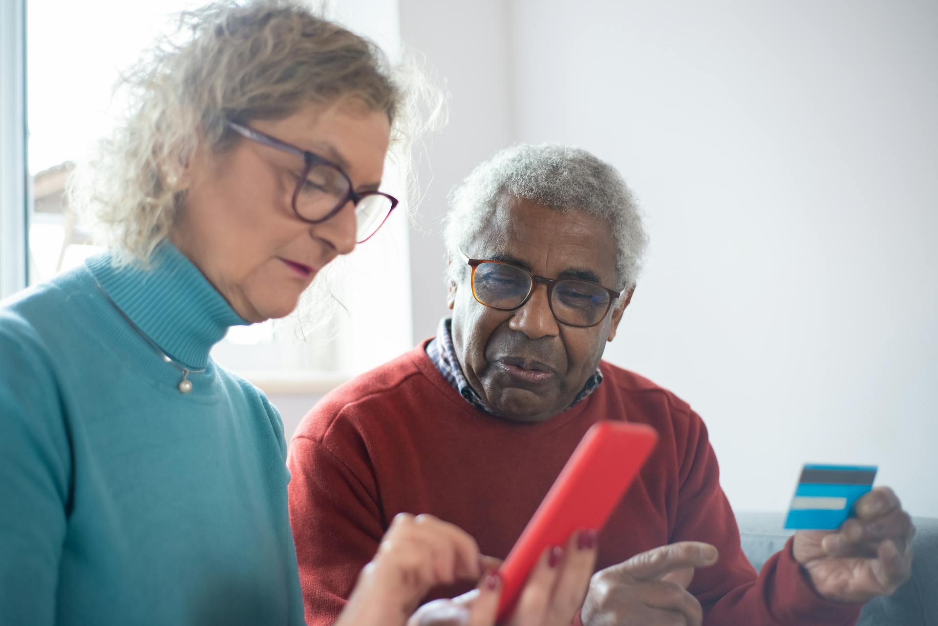 Elderly couple using smartphone and credit card for online shopping indoors.